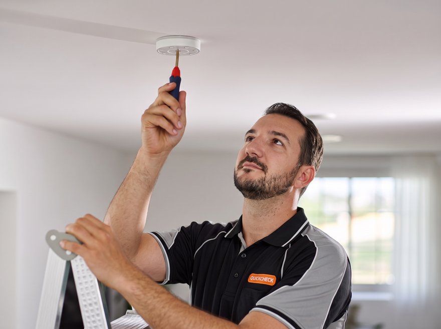 Andy, a licensed Quickcheck electrician, installing an interconnected photoelectric smoke alarm on a ceiling