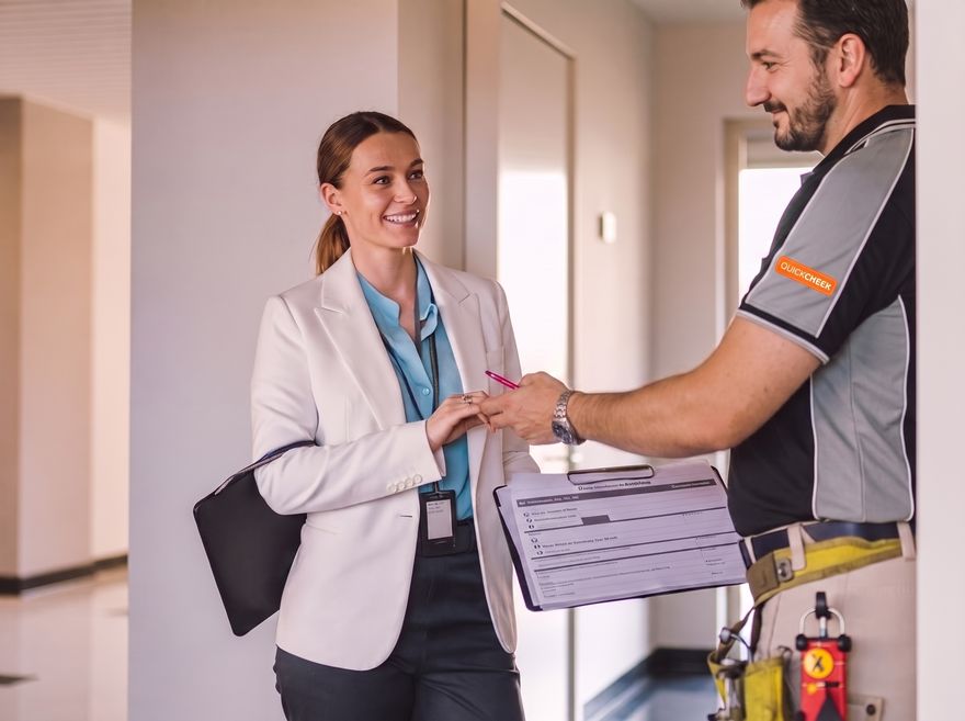 A property manager reviewing a smoke alarm compliance report with a Quickcheck electrician